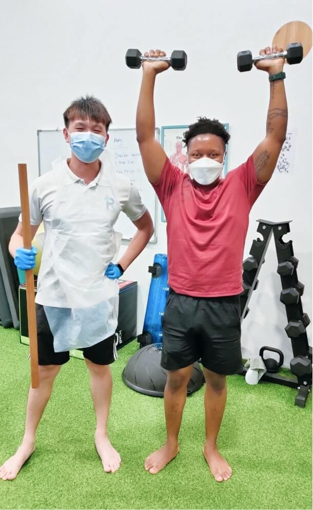 Jaffery and the patient in the center, one with a stick and the other raising a dumbbell, both wearing masks.